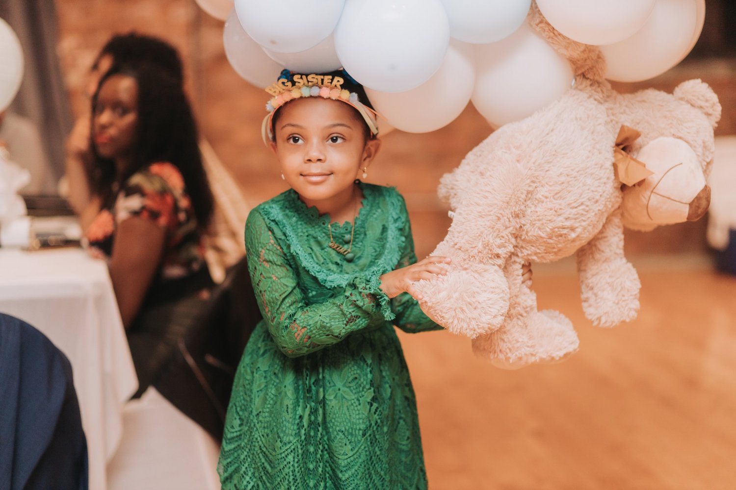 Young child in a green outfit at a family celebration with balloons.