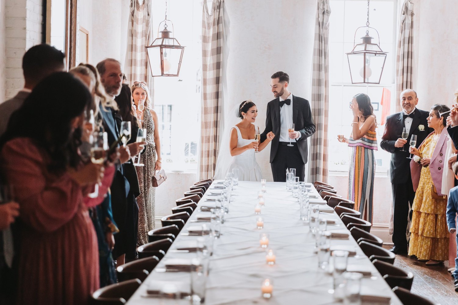 Wedding guests gather around a candlelit reception table as the newlyweds greet them.