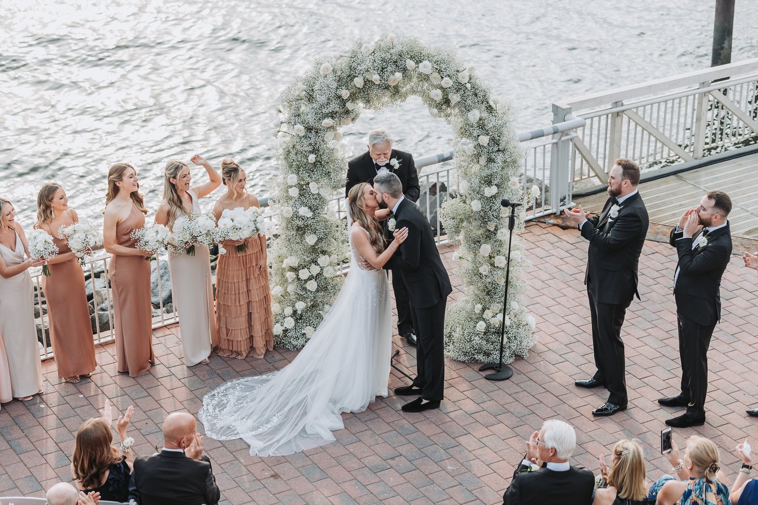 Bride and groom share a moment beneath a floral arch at their waterfront ceremony.